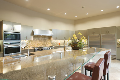 The image shows a modern, upscale kitchen with white cabinets, granite countertops, stainless steel appliances, recessed lighting, and a large island with leather bar stools.